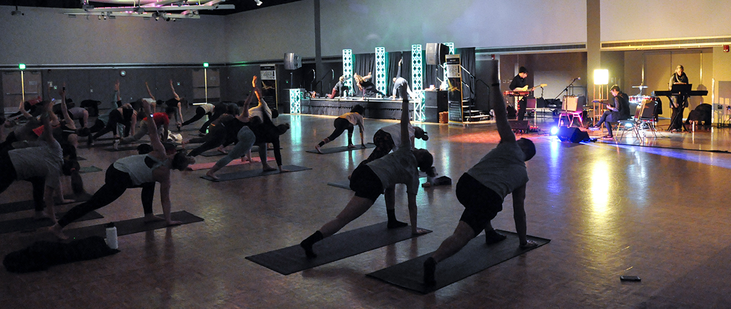 Large number of students doing yoga while few students play music in the background