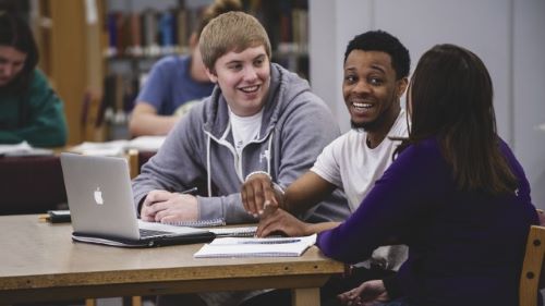 Three students studying and conversing at a table with laptop in Memorial Library