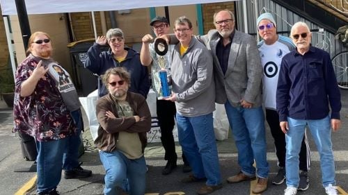 KMSU staff and volunteers posing outside at the arts center parking lot with a soundclash trophy