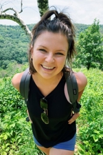 Anna Hagan posing outside for a photo with a backpack on during hiking up a brushy trail