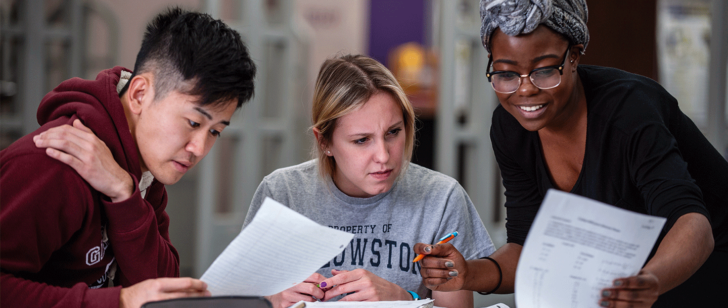 Two female students and a male student at a table studying and looking through their notes