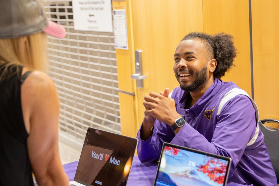 a person in purple jacket sitting at a table with laptops