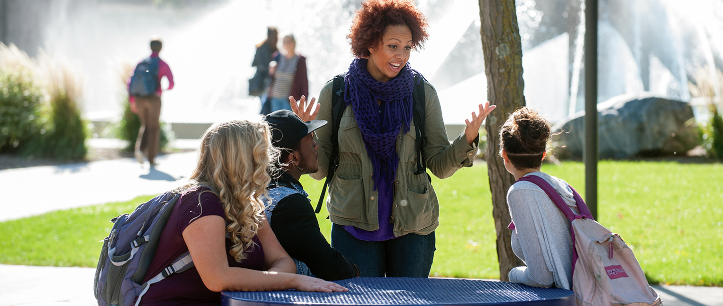 Group of students taking outside at table by the fountain