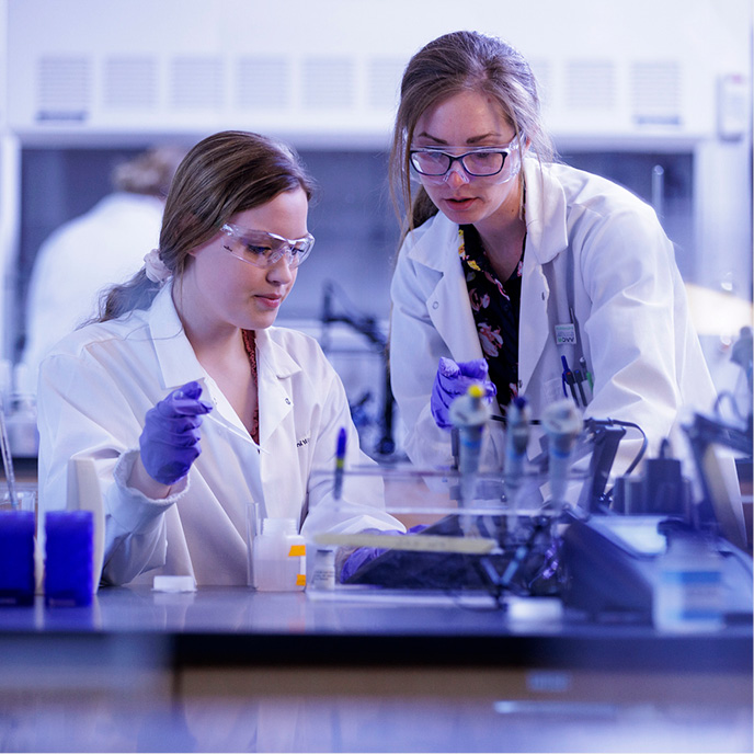 Two female students with white coats working with samples in a science lab 