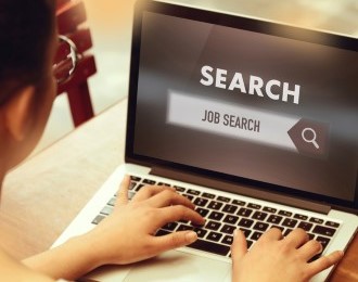 A student at a desk with laptop with job search typed in the search bar