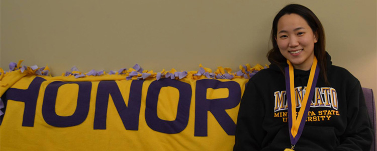 A young woman sits on a couch that has the word honors written across it.