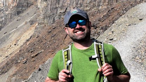 Phil Larson posing outside on a rocky mountain side with a backpack and a smile