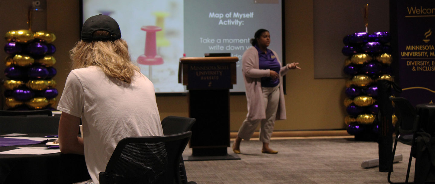 A person presenting with another person sitting at a table listening to the presentation