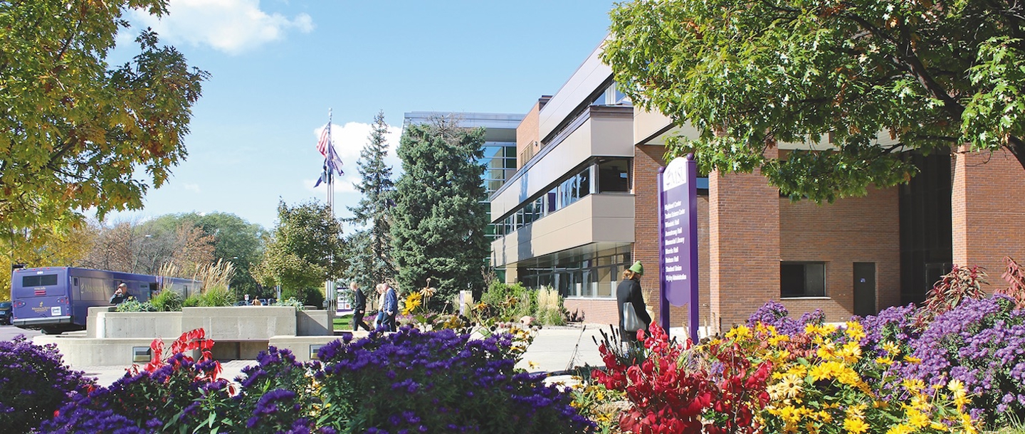 Outside the Wigley Administration building with a bus and students walking on a sunny day