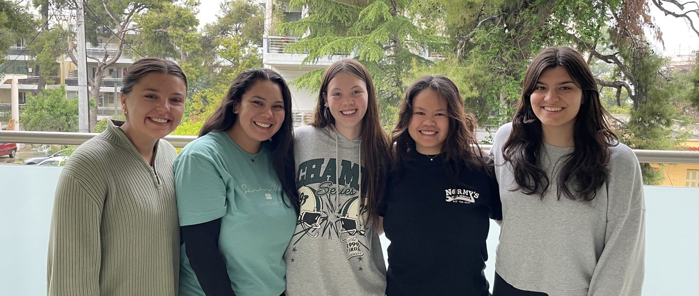 ACG First Cohort students posing for a photo on a balcony with apartments and trees in the background