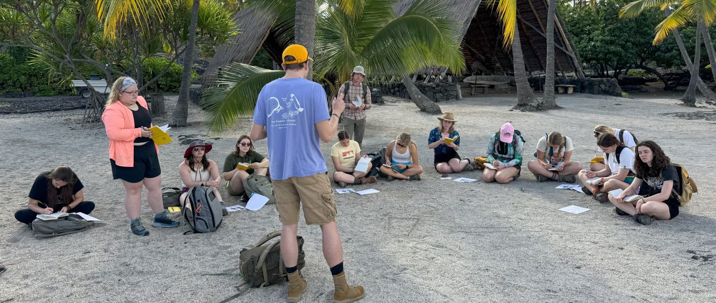 Center for Global Engagement students taking notes outside during a lecture at a tropical meeting area