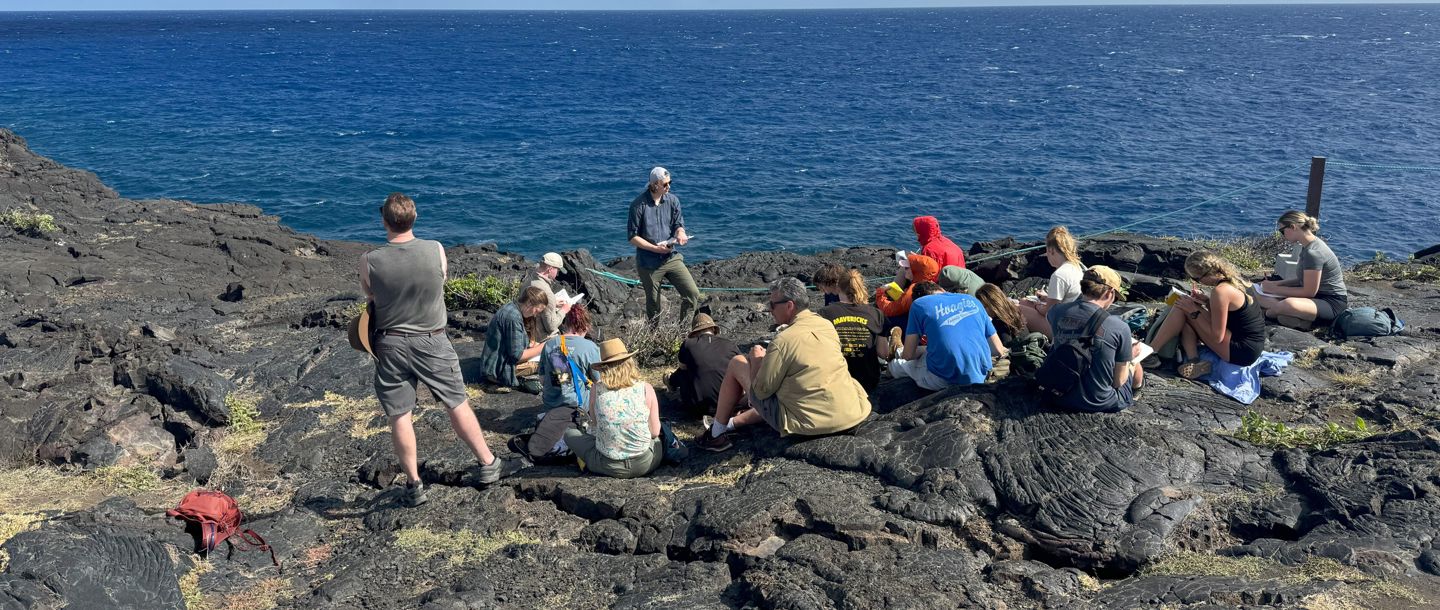 Students having a lecture on the cliff of the Papokolea Green Sand Beach in Hawaii on a sunny day with the ocean in the background