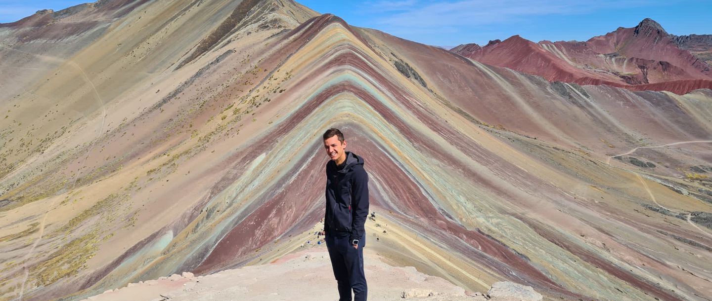 Student Jeroen standing on a hillside posing with Rainbow Mountain in the background