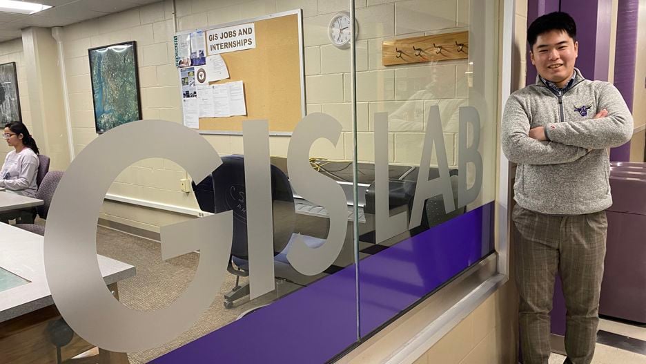  Grad student and upcoming Ph.D. candidate Masaki Hara posing with his arms folded and a smile outside the entrance to the GIS Lab on campus