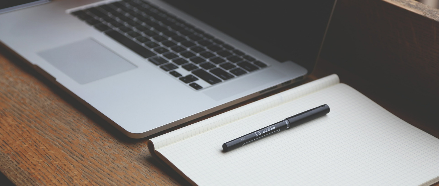 Laptop beside a notebook with a pen on a desk