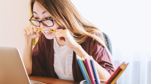 Student using laptop and biting her pencil