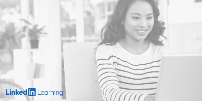 Woman working on a laptop and smiling. LinkedIn Learning logo.