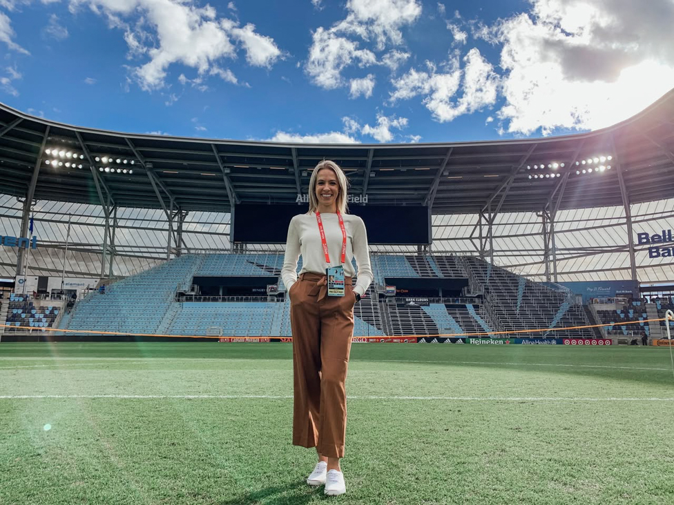 Women standing outside on a sports field, smiling.