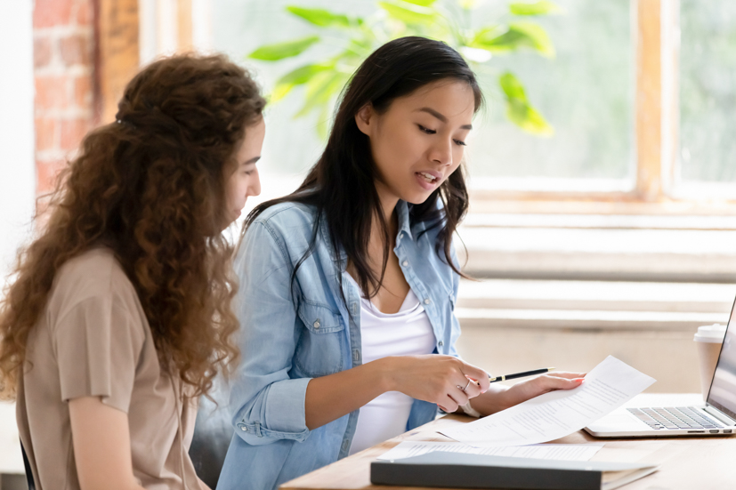 Two people sitting at a table looking over paperwork. 