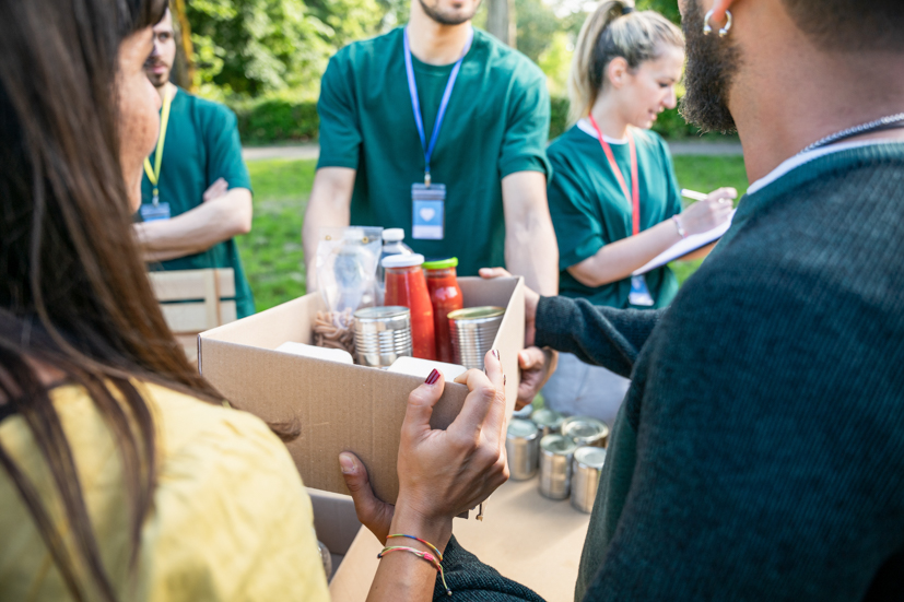 Two people holding a small box of food, handing it off to share with others.