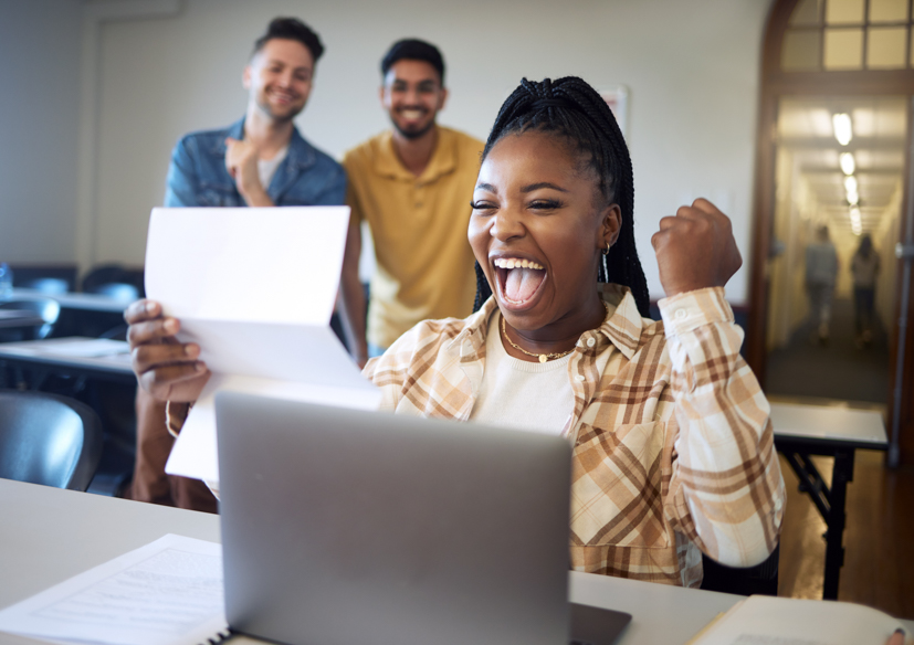 Women sitting in front of a laptop with her hand in the air, excited, looking at the computer. 