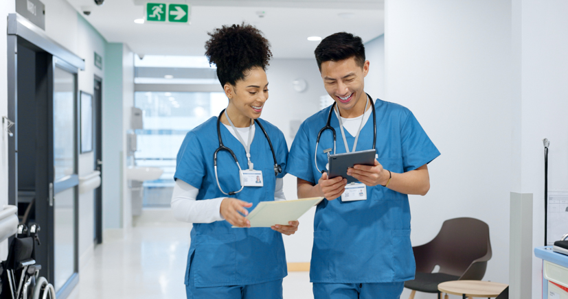 Two nurses walking through hallway talking to each other. 