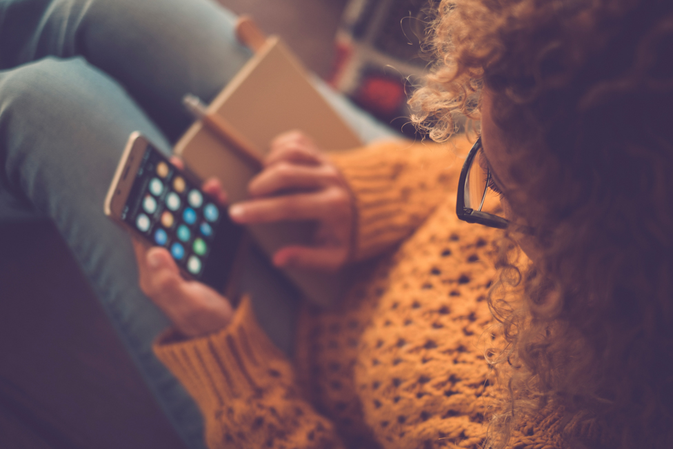 Women sitting on floor looking at her phone, about to use an app. 