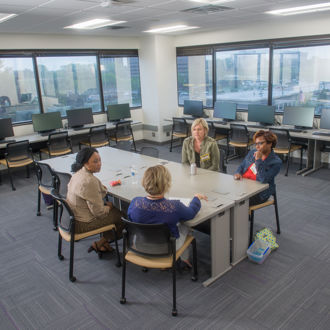 Four women sitting at a table in a classroom having a discussion