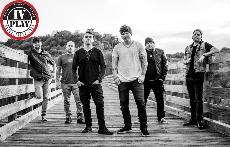 The IV Play band members posing outside on a bridge