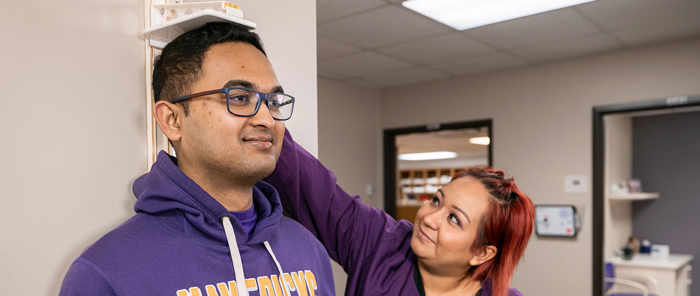 A Student Health Services nurse measuring the height of a male student patient