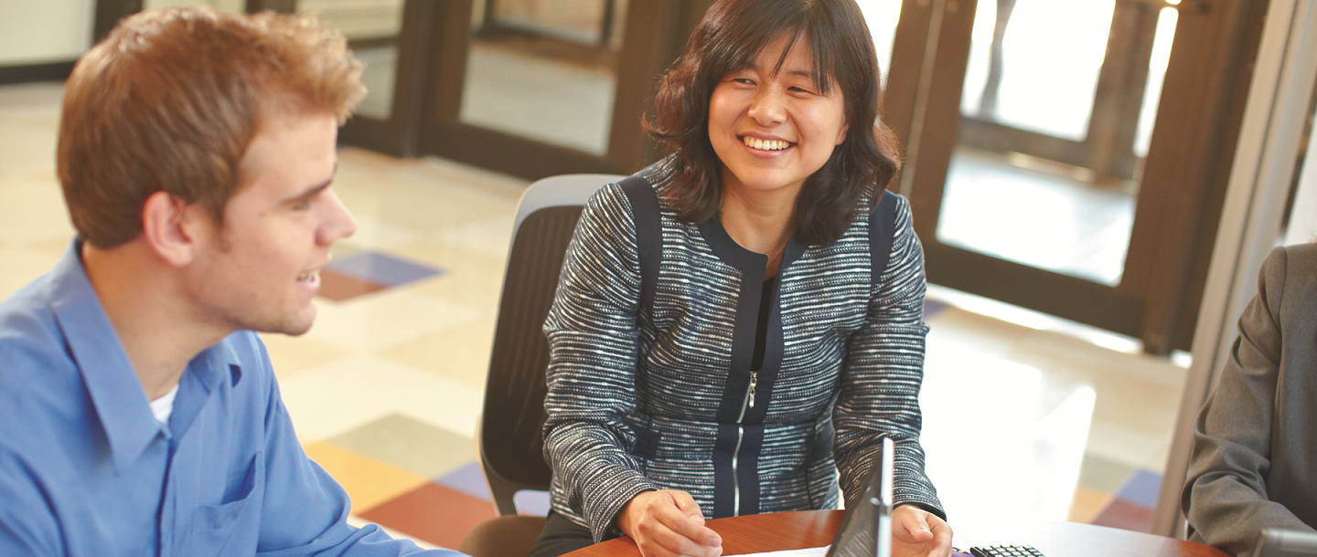 Female, Asian nontraditional student smiling, sitting next to Caucasian male student in what appears to be a classroom