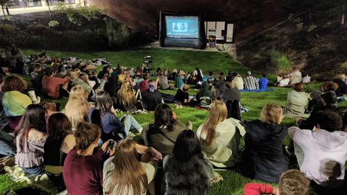 people watching a movie outdoors on campus on the valley area in front right by the horse shoe parking lot