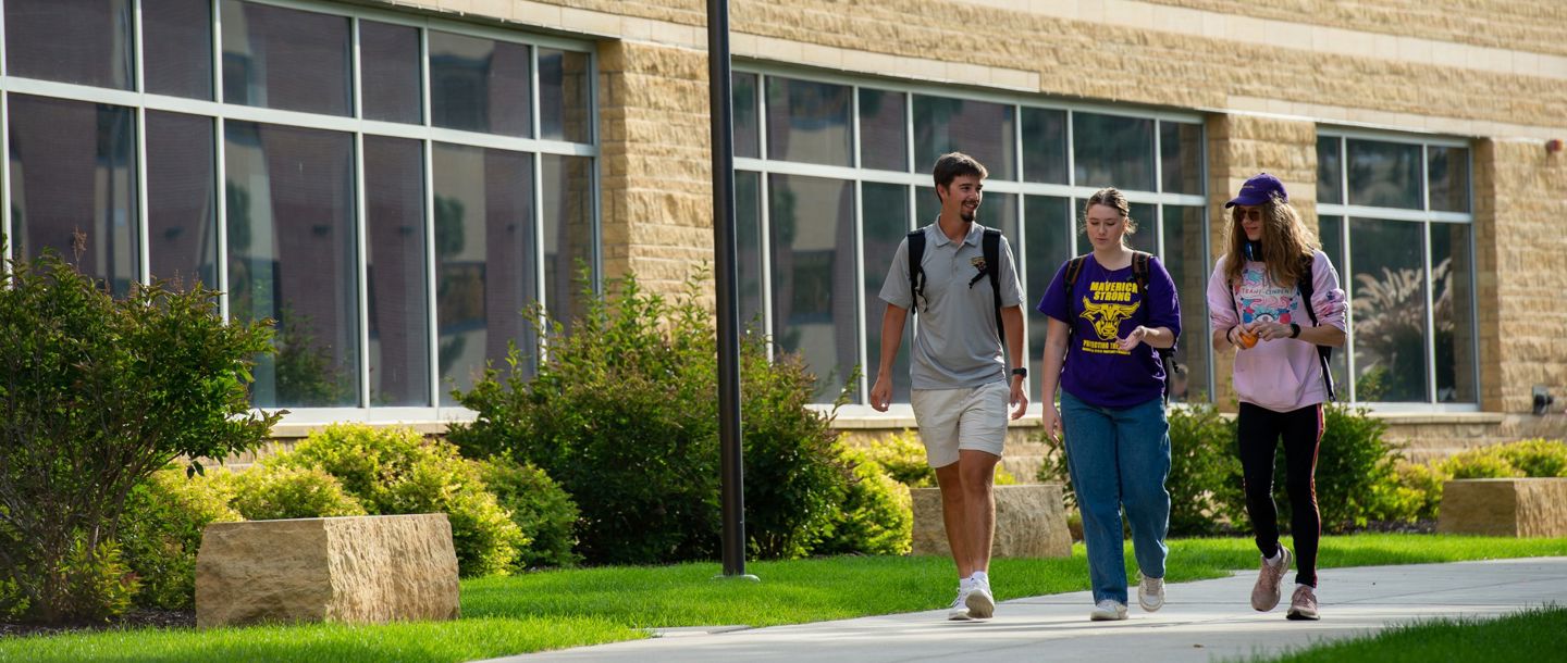 Three students walking outside on campus and talking to each other