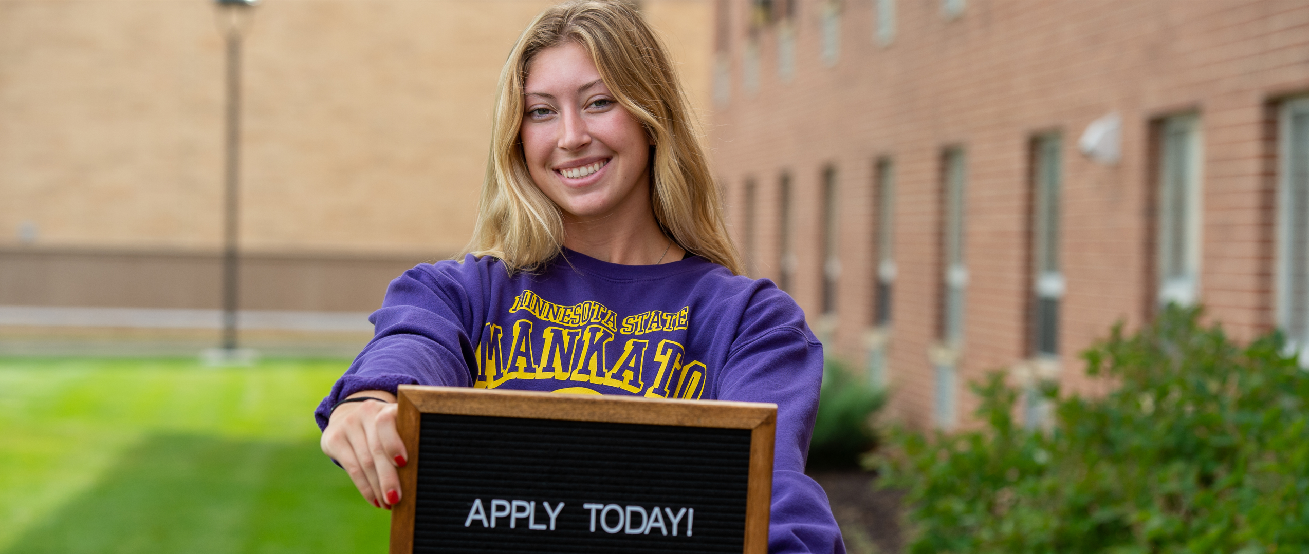 Female student holding a sign that says "Apply Today"