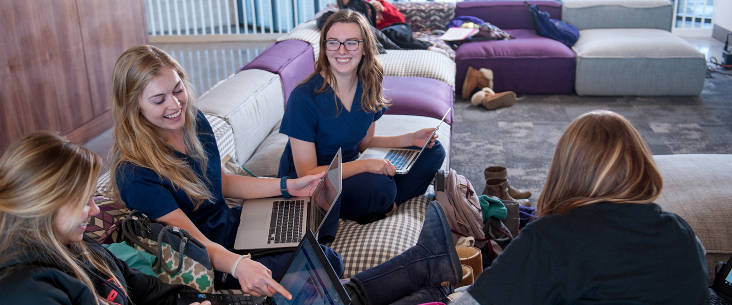 Four college girls sitting in a couch and studying on their laptop